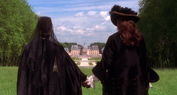 Movie still from “The Man in the Iron Mask” (1998), directed by Randall Wallace – Two people holding hands in front of a large building; Medium shot, Over the shoulder angle
