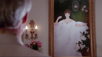 Movie still from “The Man with Two Brains” (1983), directed by Carl Reiner – A painting of a woman in a white dress next to a wall with two candles; Close Up shot, Over the shoulder angle