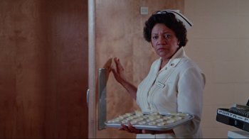 Movie still from “The Man with Two Brains” (1983), directed by Carl Reiner – A woman holding a tray of cookies and a large knife; Medium shot, Low angle