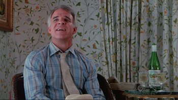 Movie still from “The Man with Two Brains” (1983), directed by Carl Reiner – A man wearing a tie sitting in front of a floral wallpaper; Medium shot, Low angle