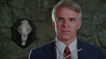 Movie still from “The Man with Two Brains” (1983), directed by Carl Reiner – A man in a suit and red tie holding a white stick; Close Up shot, Over the shoulder angle