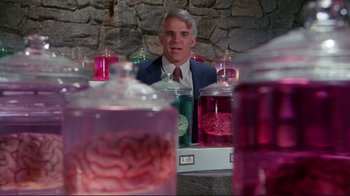 Movie still from “The Man with Two Brains” (1983), directed by Carl Reiner – A man sitting in front of a bunch of jars; Medium shot, Over the shoulder angle
