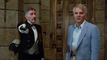 Movie still from “The Man with Two Brains” (1983), directed by Carl Reiner – Two men standing next to each other in front of a wooden door; Medium shot, Over the shoulder angle