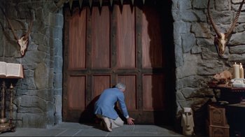 Movie still from “The Man with Two Brains” (1983), directed by Carl Reiner – A man kneeling down in front of a wooden door; Wide shot, High angle