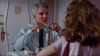 Movie still from “The Man with Two Brains” (1983), directed by Carl Reiner – A man holding a cup of coffee in front of a woman at a table; Medium shot, Over the shoulder angle