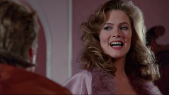 Movie still from “The Man with Two Brains” (1983), directed by Carl Reiner – A woman in a purple robe smiling for the camera; Close Up shot, Over the shoulder angle