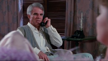 Movie still from “The Man with Two Brains” (1983), directed by Carl Reiner – An older man talking on a phone while sitting in a chair; Medium shot, Over the shoulder angle