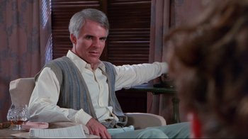 Movie still from “The Man with Two Brains” (1983), directed by Carl Reiner – An older man sitting in a chair holding a book; Medium shot, Over the shoulder angle