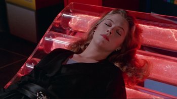 Movie still from “The Man with Two Brains” (1983), directed by Carl Reiner – A woman laying on top of a red bench; Medium shot, High angle