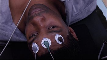 Movie still from “The Manchurian Candidate” (2004), directed by Jonathan Demme – A man is laying on the ground with some wires attached to his ears; Close Up shot, Overhead angle