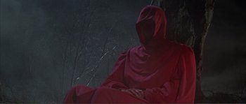 Movie still from “The Masque of the Red Death” (1964), directed by Roger Corman – A person in a red robe sitting on a bench; Wide shot, High angle