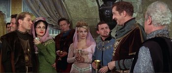 Movie still from “The Masque of the Red Death” (1964), directed by Roger Corman – A group of people standing around a woman in medieval garb; Medium shot, Over the shoulder angle