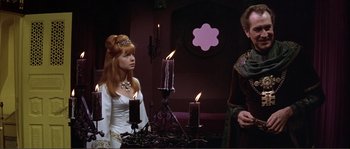 Movie still from “The Masque of the Red Death” (1964), directed by Roger Corman – A woman standing next to a man in front of candles on a table; Medium shot, Low angle