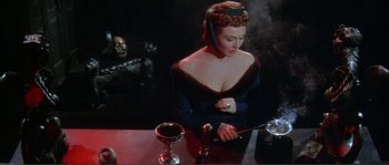 Movie still from “The Masque of the Red Death” (1964), directed by Roger Corman – A woman is smoking a cigarette in front of a wine glass; Medium shot, High angle