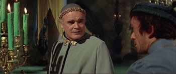 Movie still from “The Masque of the Red Death” (1964), directed by Roger Corman – An older man wearing a green coat and a gold crown; Close Up shot, Over the shoulder angle