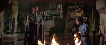 Movie still from “The Masque of the Red Death” (1964), directed by Roger Corman – A man standing in front of a fireplace with candles; Wide shot, High angle