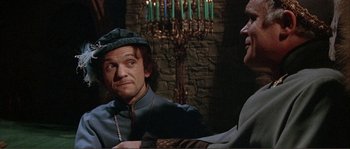 Movie still from “The Masque of the Red Death” (1964), directed by Roger Corman – A man wearing a green hat and a blue jacket; Medium shot, Over the shoulder angle