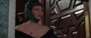 Movie still from “The Masque of the Red Death” (1964), directed by Roger Corman – A woman with a cross on her chest and a green head scarf; Close Up shot, Over the shoulder angle