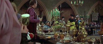 Movie still from “The Masque of the Red Death” (1964), directed by Roger Corman – A group of people sitting around a table with food on top of it; Wide shot, Over the shoulder angle