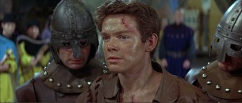 Movie still from “The Masque of the Red Death” (1964), directed by Roger Corman – A man with a bandage on his face and a helmet on his head; Close Up shot, Over the shoulder angle