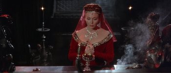 Movie still from “The Masque of the Red Death” (1964), directed by Roger Corman – A woman in a red dress holding a wine goblet; Medium shot, High angle