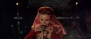 Movie still from “The Masque of the Red Death” (1964), directed by Roger Corman – A woman in a red dress is holding a cup; Close Up shot, High angle