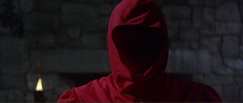 Movie still from “The Masque of the Red Death” (1964), directed by Roger Corman – A person in a red hooded sweatshirt is sitting in front of a brick wall; Close Up shot, Low angle