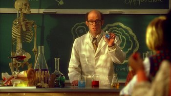 Movie still from “The Master of Disguise” (2002), directed by Perry Andelin Blake – A man in a white lab coat holding a glass in front of a chalkboard; Medium shot, Over the shoulder angle