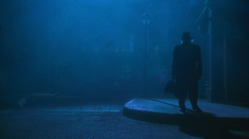 Movie still from “The Master of Disguise” (2002), directed by Perry Andelin Blake – A man in a black hat and a black suit walking on a street; Wide shot, Low angle