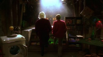 Movie still from “The Master of Disguise” (2002), directed by Perry Andelin Blake – Two people are standing in a room looking at a light; Wide shot, Over the shoulder angle