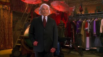 Movie still from “The Master of Disguise” (2002), directed by Perry Andelin Blake – A man in a suit and tie standing in a room; Medium shot, Over the shoulder angle