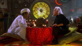 Movie still from “The Master of Disguise” (2002), directed by Perry Andelin Blake – Two people sitting at a table in front of a clock; Medium shot, High angle