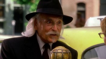 Movie still from “The Master of Disguise” (2002), directed by Perry Andelin Blake – An old man with a beard and a hat is holding a microphone; Close Up shot, Over the shoulder angle