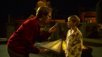 Movie still from “The Master of Disguise” (2002), directed by Perry Andelin Blake – A man and a boy are standing next to each other in front of a building; Medium shot, Over the shoulder angle