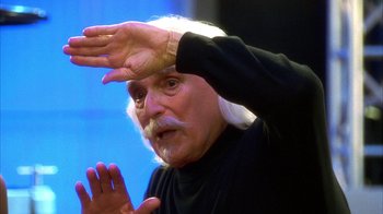 Movie still from “The Master of Disguise” (2002), directed by Perry Andelin Blake – An older man with white hair and a white beard is holding his hands up; Close Up shot, Low angle