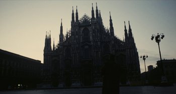 Movie still from “The Mattei Affair” (1972), directed by Francesco Rosi – A couple of people standing in front of a large building; Extreme Wide shot, Low angle
