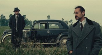 Movie still from “The Mattei Affair” (1972), directed by Francesco Rosi – A man standing in front of an old black car; Medium shot, Over the shoulder angle