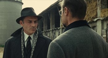 Movie still from “The Mattei Affair” (1972), directed by Francesco Rosi – A man in a hat and a suit talking to another man in a hat; Close Up shot, Over the shoulder angle