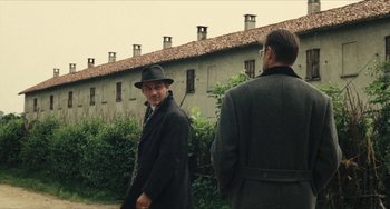 Movie still from “The Mattei Affair” (1972), directed by Francesco Rosi – A man in a hat and a coat standing next to another man in a hat; Wide shot, Over the shoulder angle