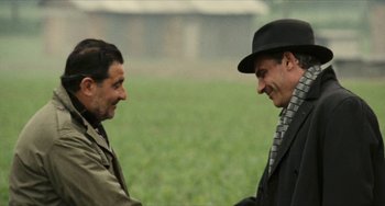 Movie still from “The Mattei Affair” (1972), directed by Francesco Rosi – Two men shaking hands in front of a field of green grass; Medium shot, Over the shoulder angle