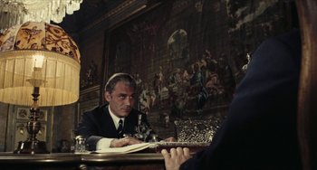 Movie still from “The Mattei Affair” (1972), directed by Francesco Rosi – A man sitting at a table in front of a painting; Medium shot, Over the shoulder angle