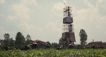 Movie still from “The Mattei Affair” (1972), directed by Francesco Rosi – A tall structure in the middle of a field of green grass; Extreme Wide shot, Low angle