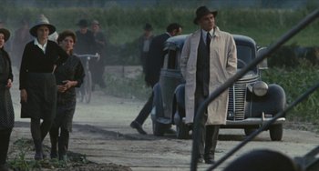 Movie still from “The Mattei Affair” (1972), directed by Francesco Rosi – A man in a trench coat and a hat walking down a street; Wide shot, Over the shoulder angle