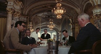 Movie still from “The Mattei Affair” (1972), directed by Francesco Rosi – A group of men sitting around a table with drinks; Wide shot, Low angle