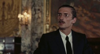 Movie still from “The Mattei Affair” (1972), directed by Francesco Rosi – A man in a suit and tie wearing glasses; Close Up shot, Over the shoulder angle