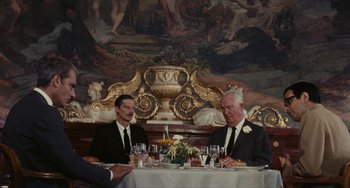 Movie still from “The Mattei Affair” (1972), directed by Francesco Rosi – Two men sitting at a dinner table in front of a painting; Medium shot, Over the shoulder angle