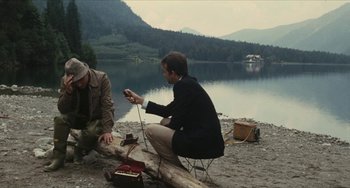 Movie still from “The Mattei Affair” (1972), directed by Francesco Rosi – Two men sitting on the ground near a body of water; Wide shot, High angle