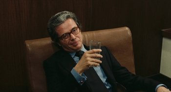 Movie still from “The Mattei Affair” (1972), directed by Francesco Rosi – A man sitting in a chair holding a glass of water; Close Up shot, Over the shoulder angle