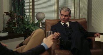 Movie still from “The Mattei Affair” (1972), directed by Francesco Rosi – A man sitting in a chair holding a glass of wine; Medium shot, Over the shoulder angle