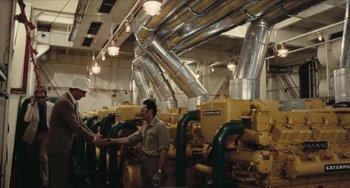 Movie still from “The Mattei Affair” (1972), directed by Francesco Rosi – Two men shaking hands in front of a large machine; Extreme Wide shot, High angle